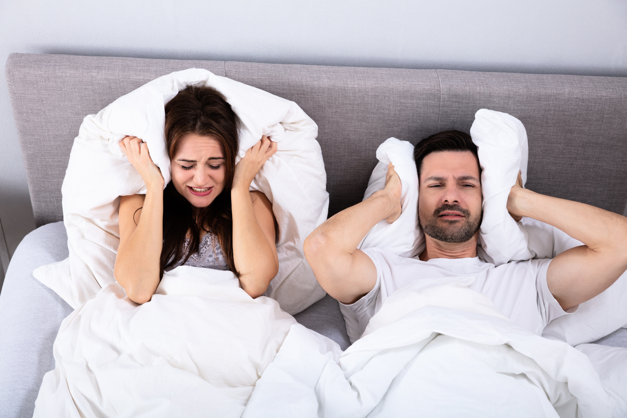 Disturbed Couple Covering Their Ears With Pillow On Bed