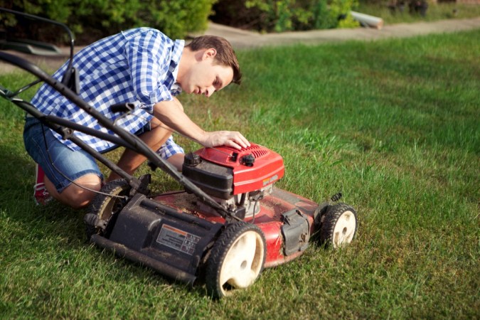 A man kneeling to check out lawn mower.