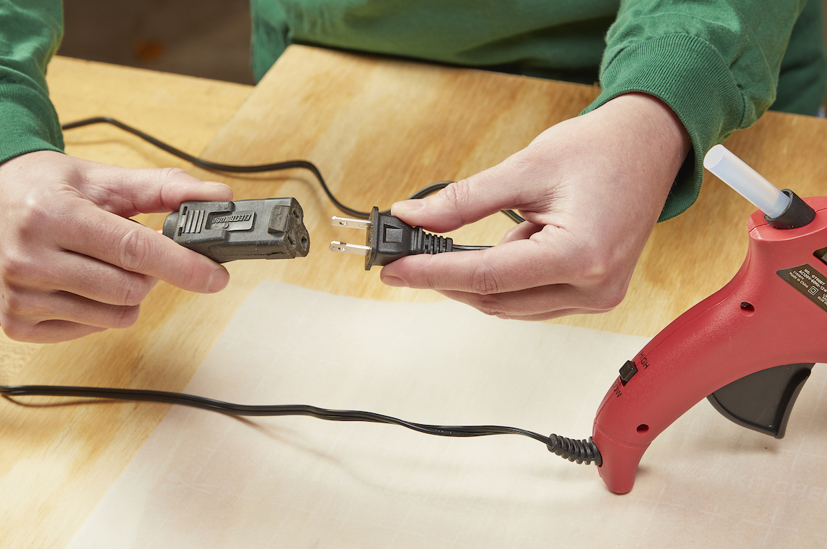 Woman plugging a hot glue gun into a black extension cord.