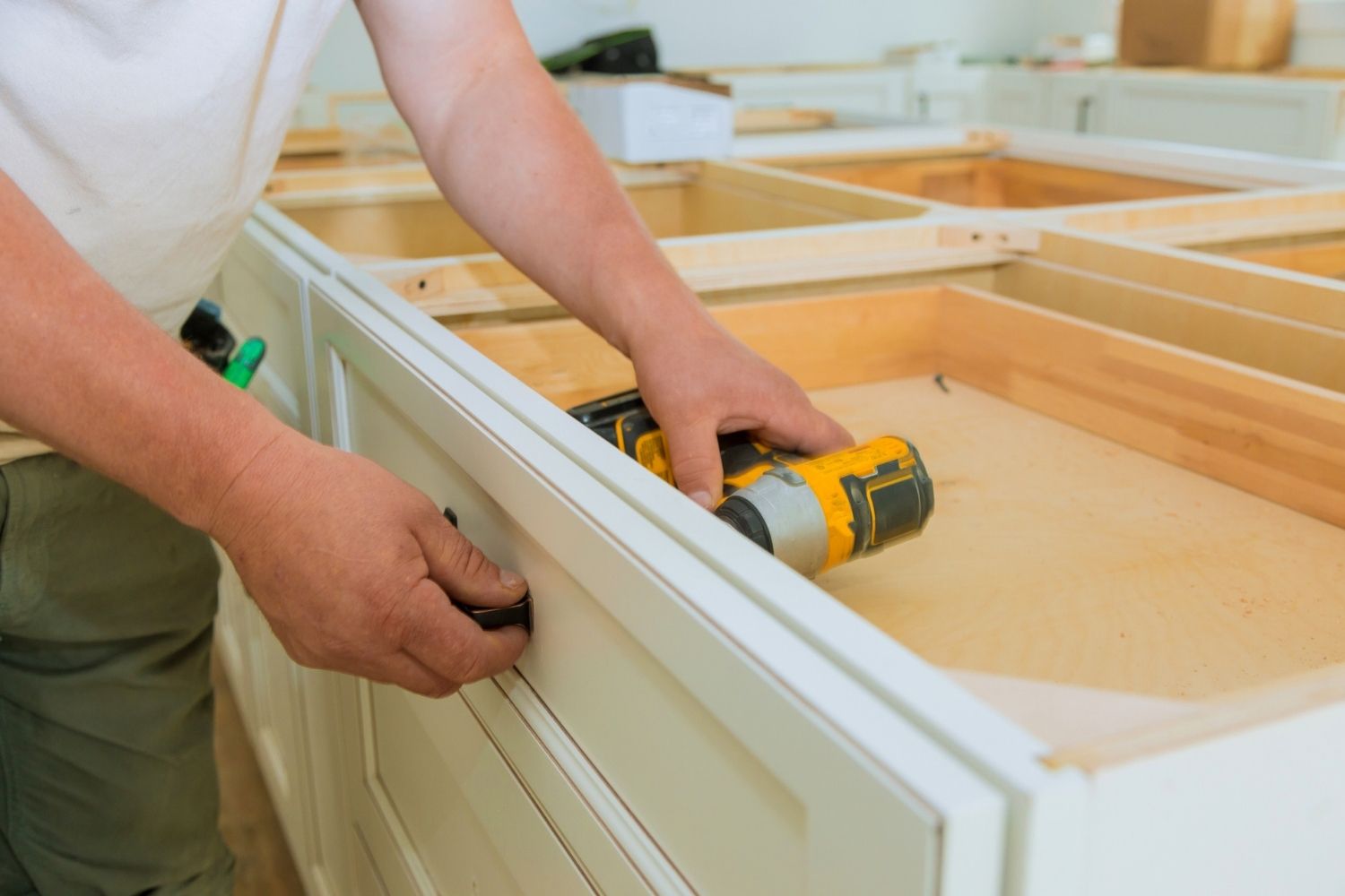 A view of a worker using a drill to refresh cabinetry.