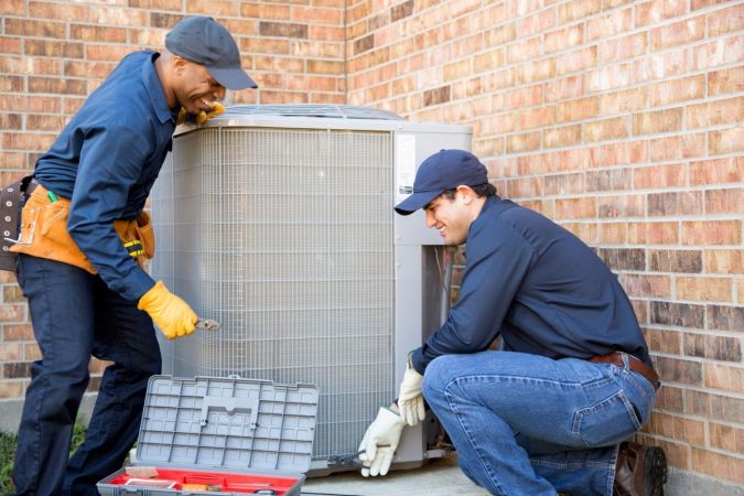 Two workers install an HVAC unit.