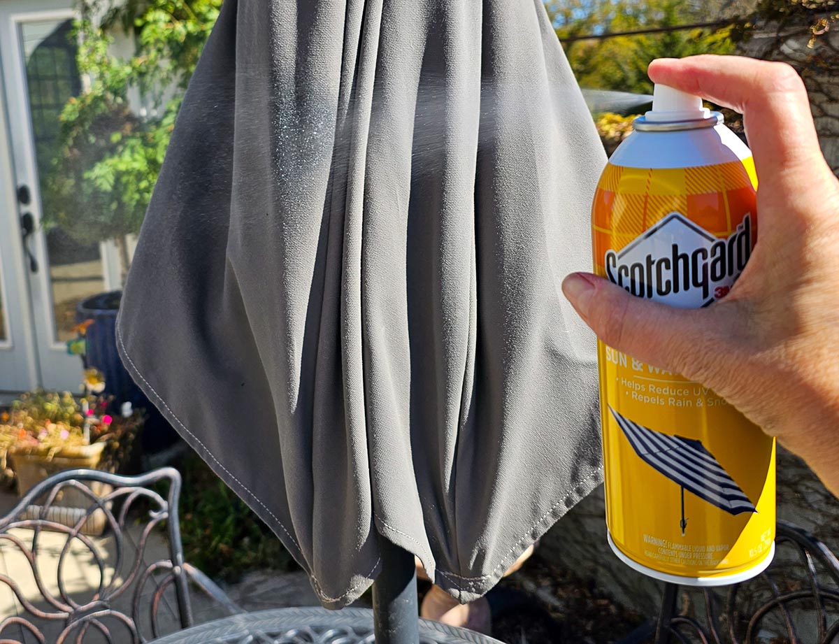 A person spraying the Scotchgard Sun & Water Shield on a grey patio umbrella.