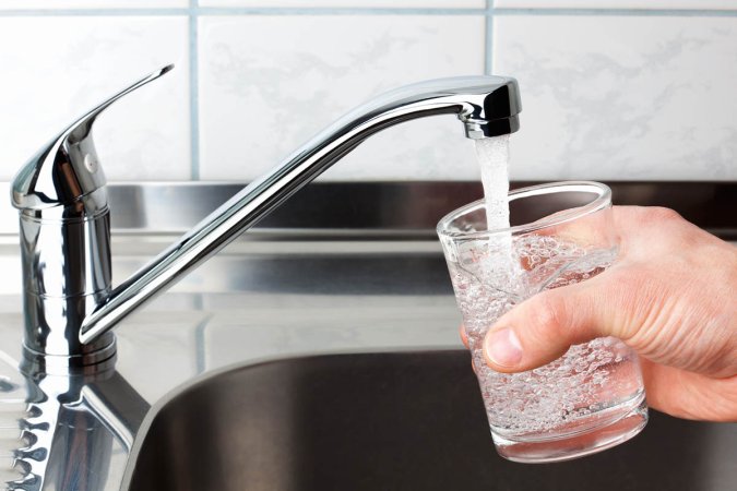 A close up of someone running a faucet to full a glass with water.