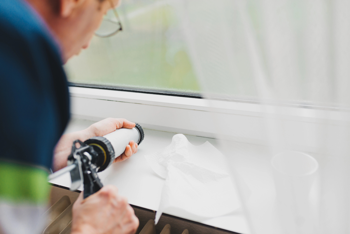 Backview of an elderly man using a silicone tube  of caulk on a windowsill.