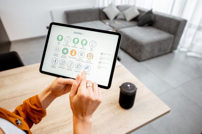 Young woman controlling home with a digital touch screen panel. Concept of a smart home and mobile application for managing smart devices at home