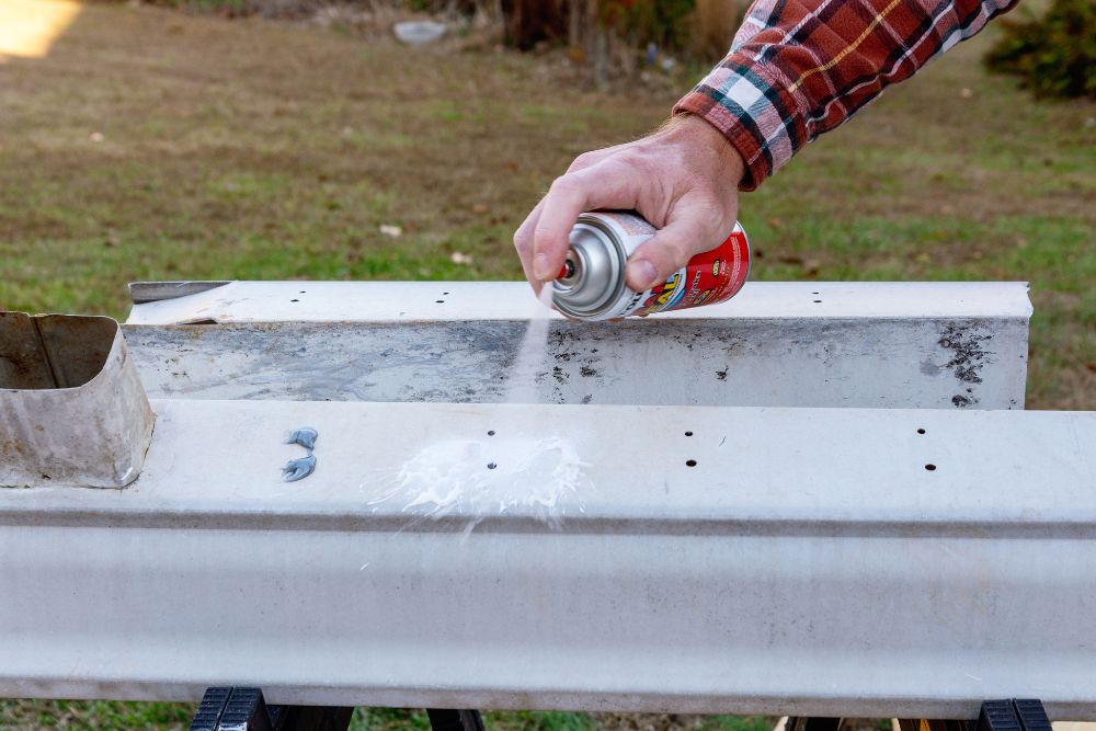 Person spraying a sealant on holes in a gutter