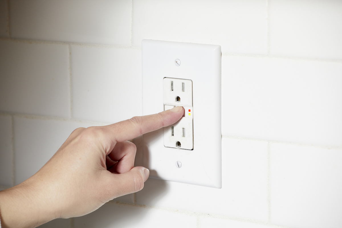 Woman tries to reset a GFCI outlet situated on a white wall.