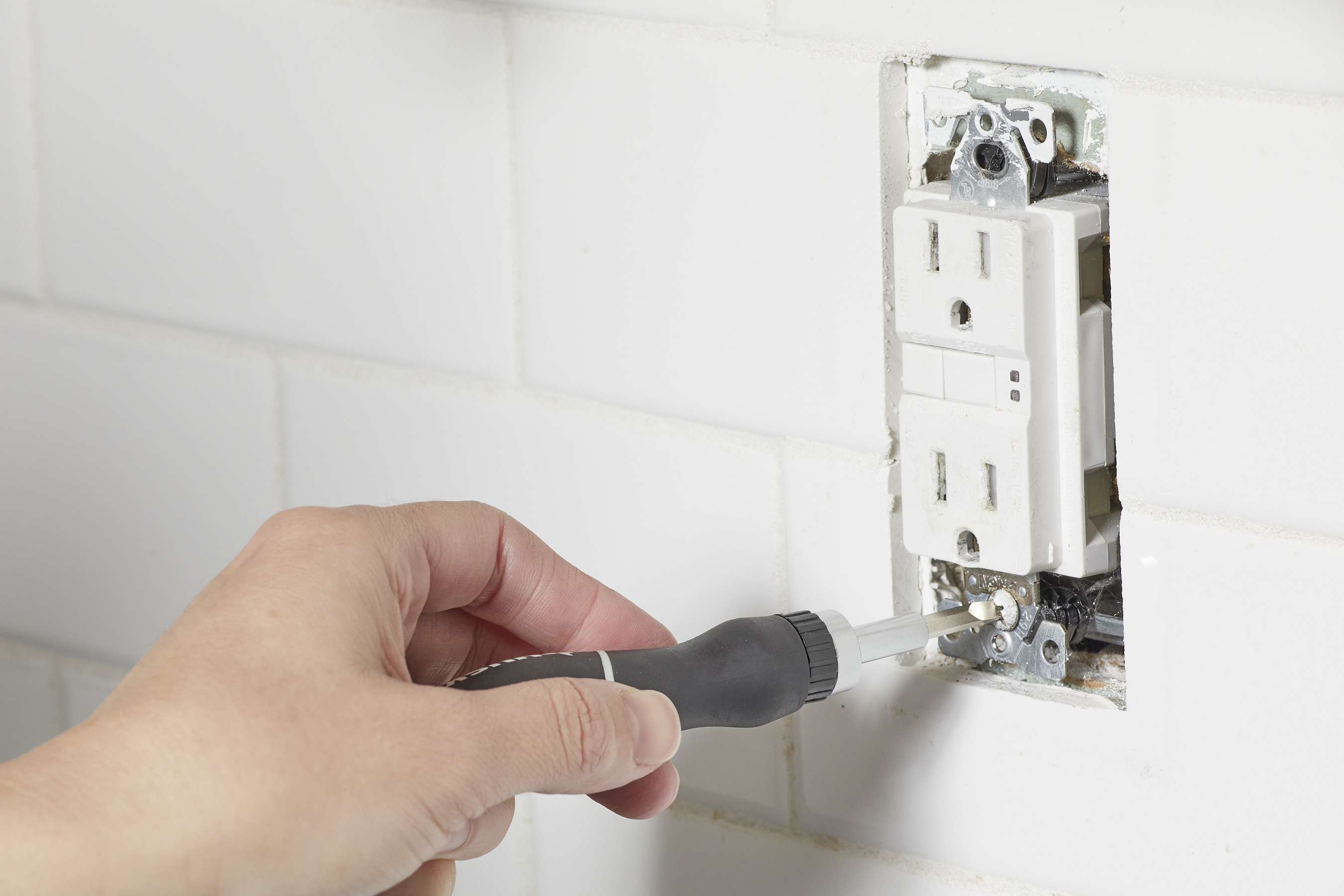 Woman unscrews the screws that hold an electrical outlet in the wall. 