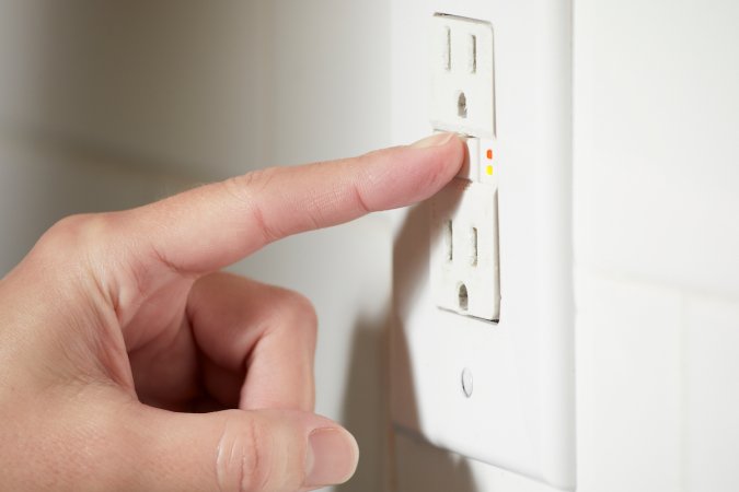 Woman pushes the test and reset buttons on a GFCI outlet.