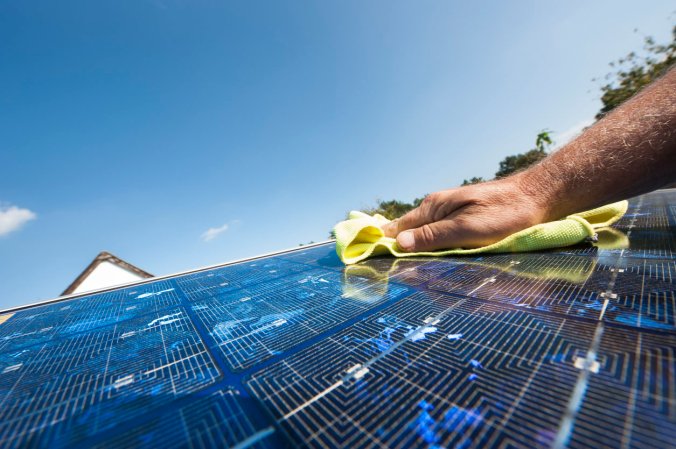 A person with only their hand visible cleans a solar panel with a yellow cloth.