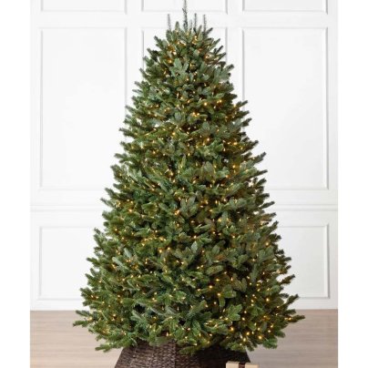 The Balsam Hill Fraser Fir Flip Tree in a dark wicker basket on a wood floor with a white paneled wall in the background.