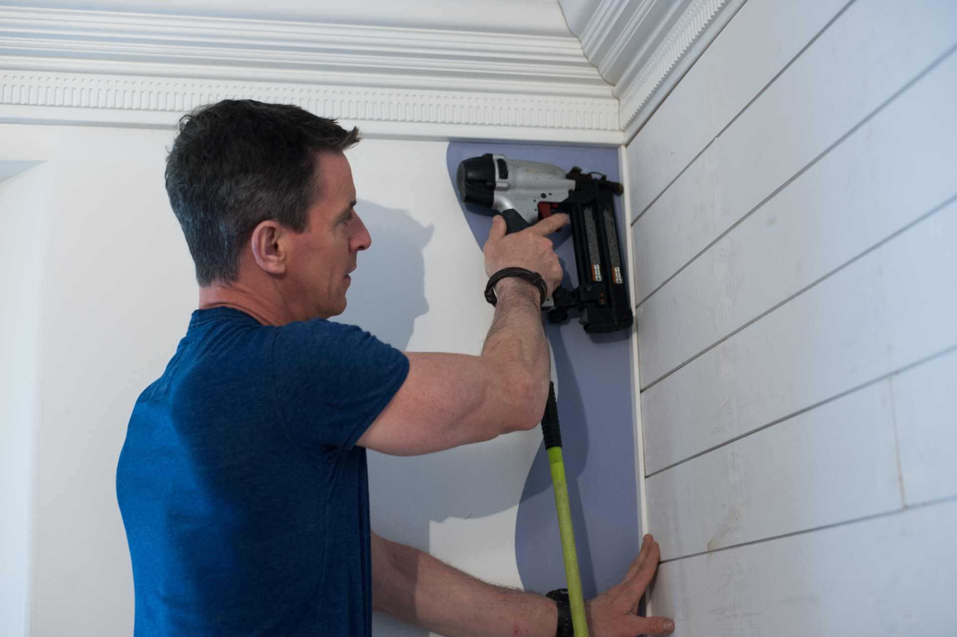 A man uses a brad nailer on a wall,