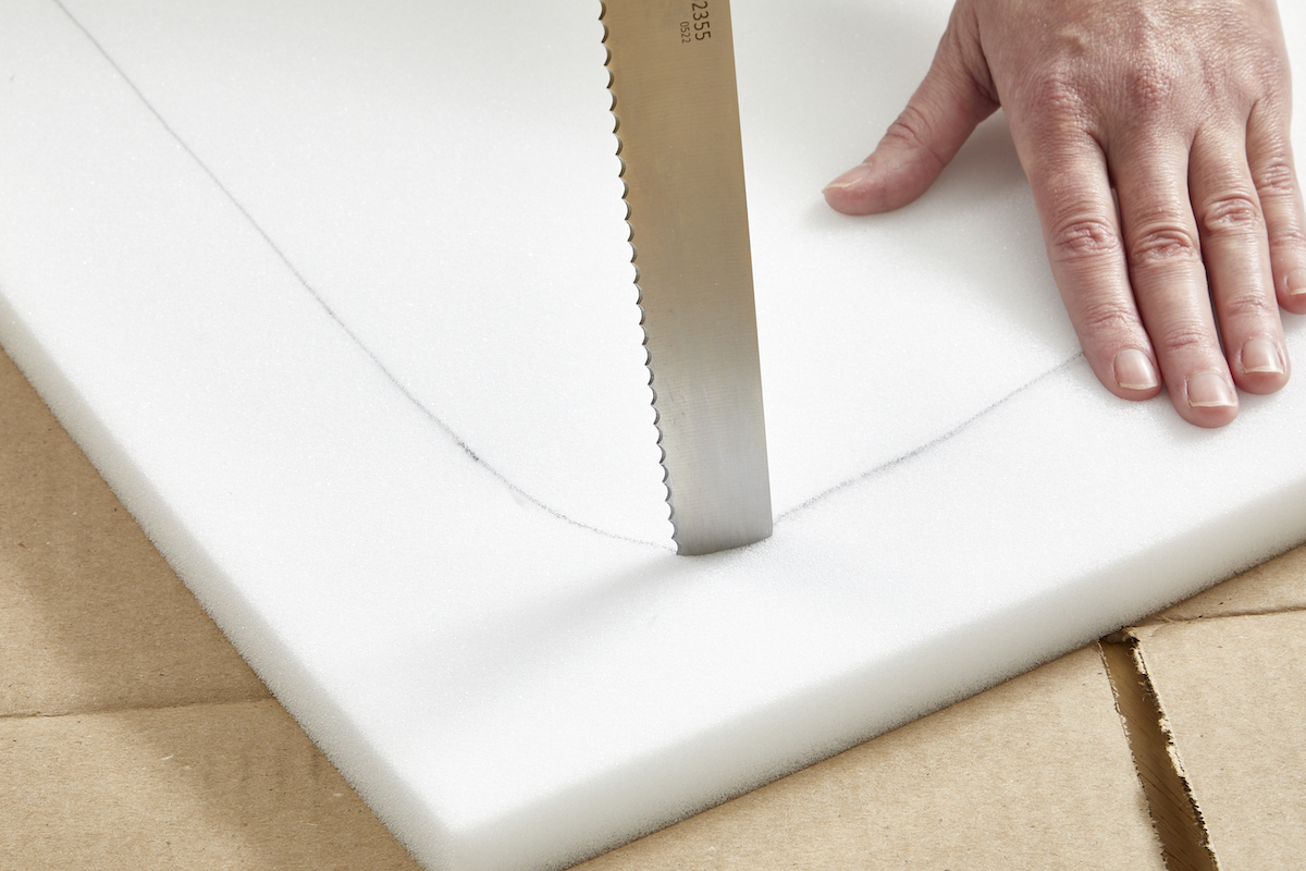 Woman using a serrated knife to cut a curve in a piece of foam.