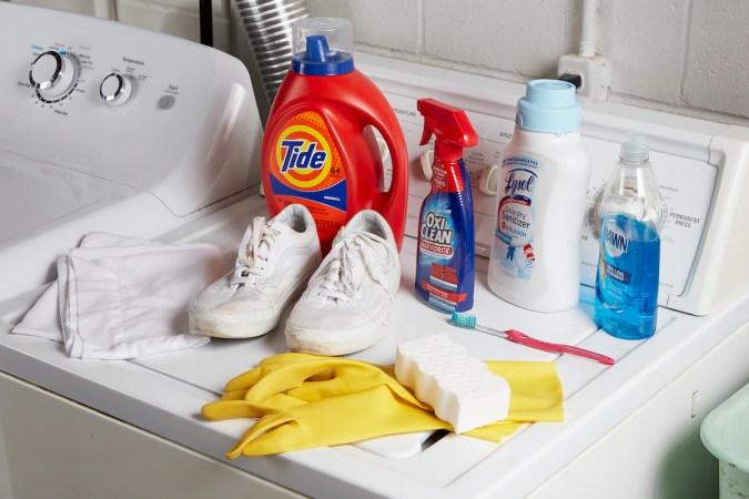 White shoes, detergent, stain remover, and other cleaning materials on top of a washing machine.