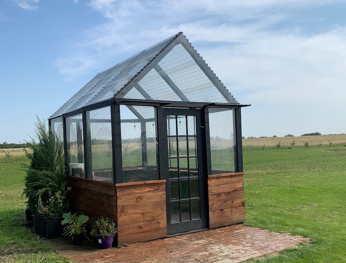 A modular greenhouse with reclaimed door in a field.