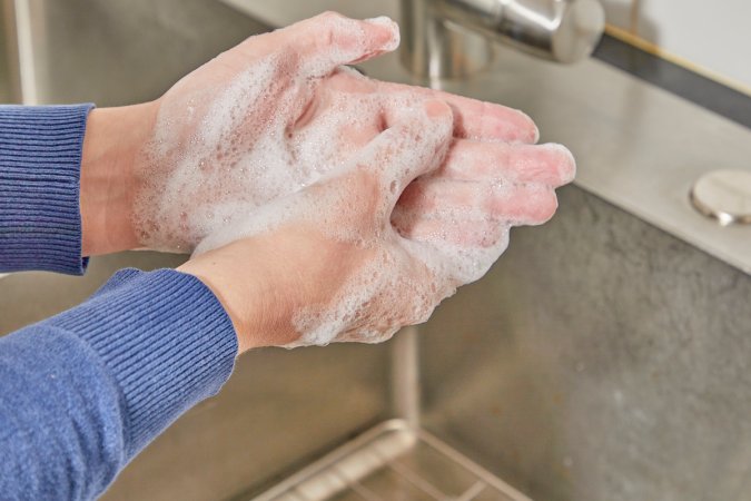 Woman washes her hands with foamy soap under a running faucet.