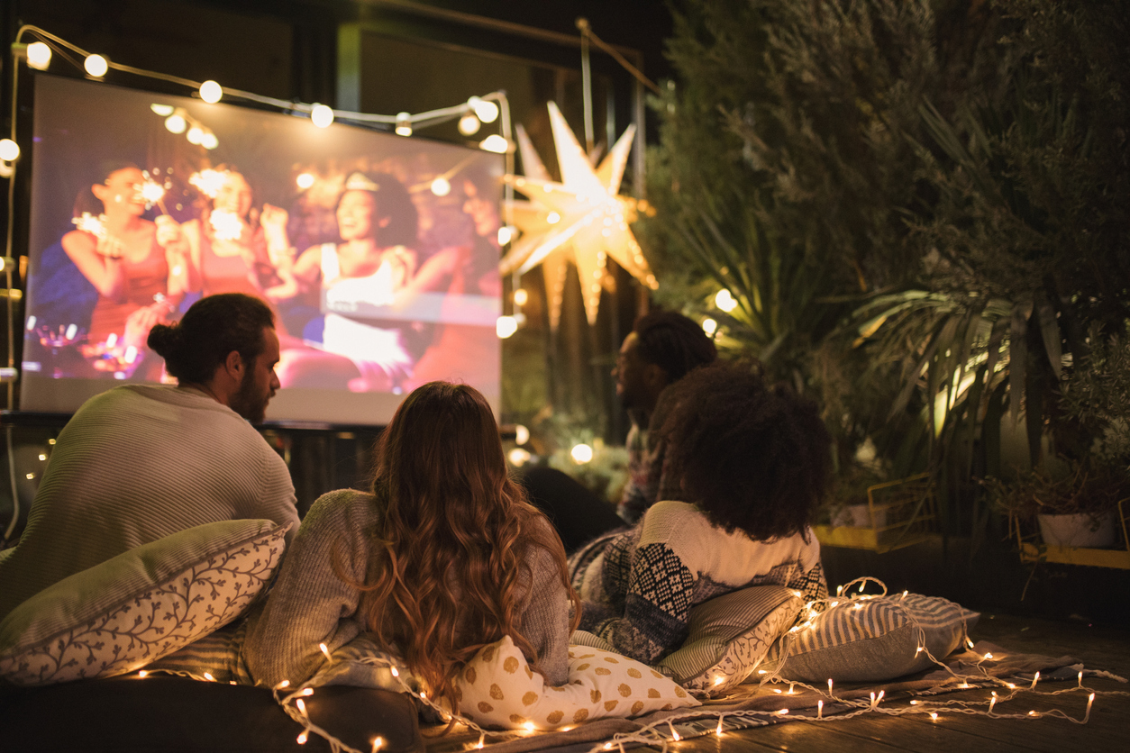 Three friends watching a movie in the backyard decorated with string lights.