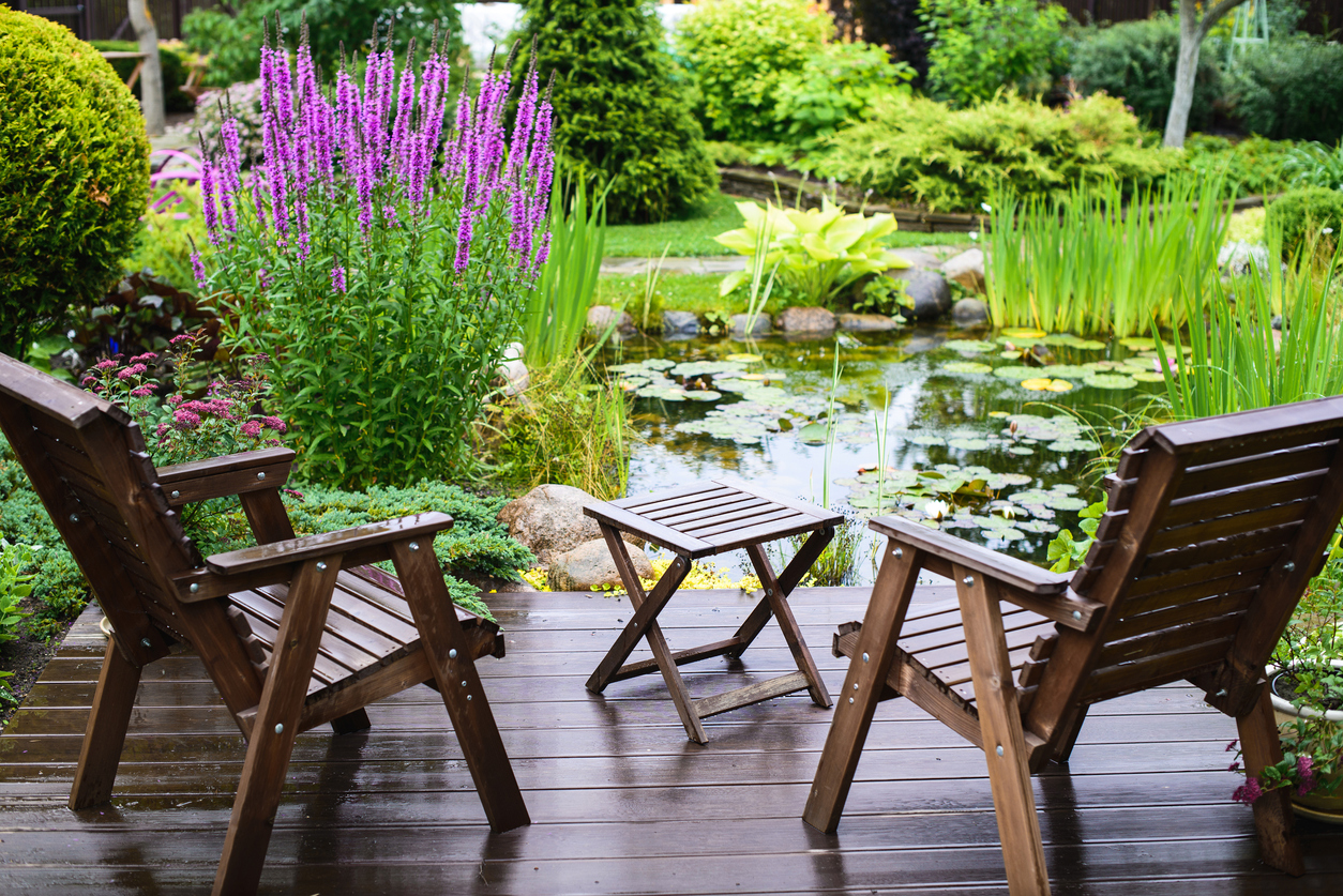 Slatted wood patio set with a view of a backyard pond.