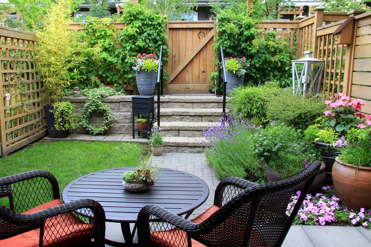 A small backyard garden full of flower beds and container plants, with steps and handrails to the backyard gate.