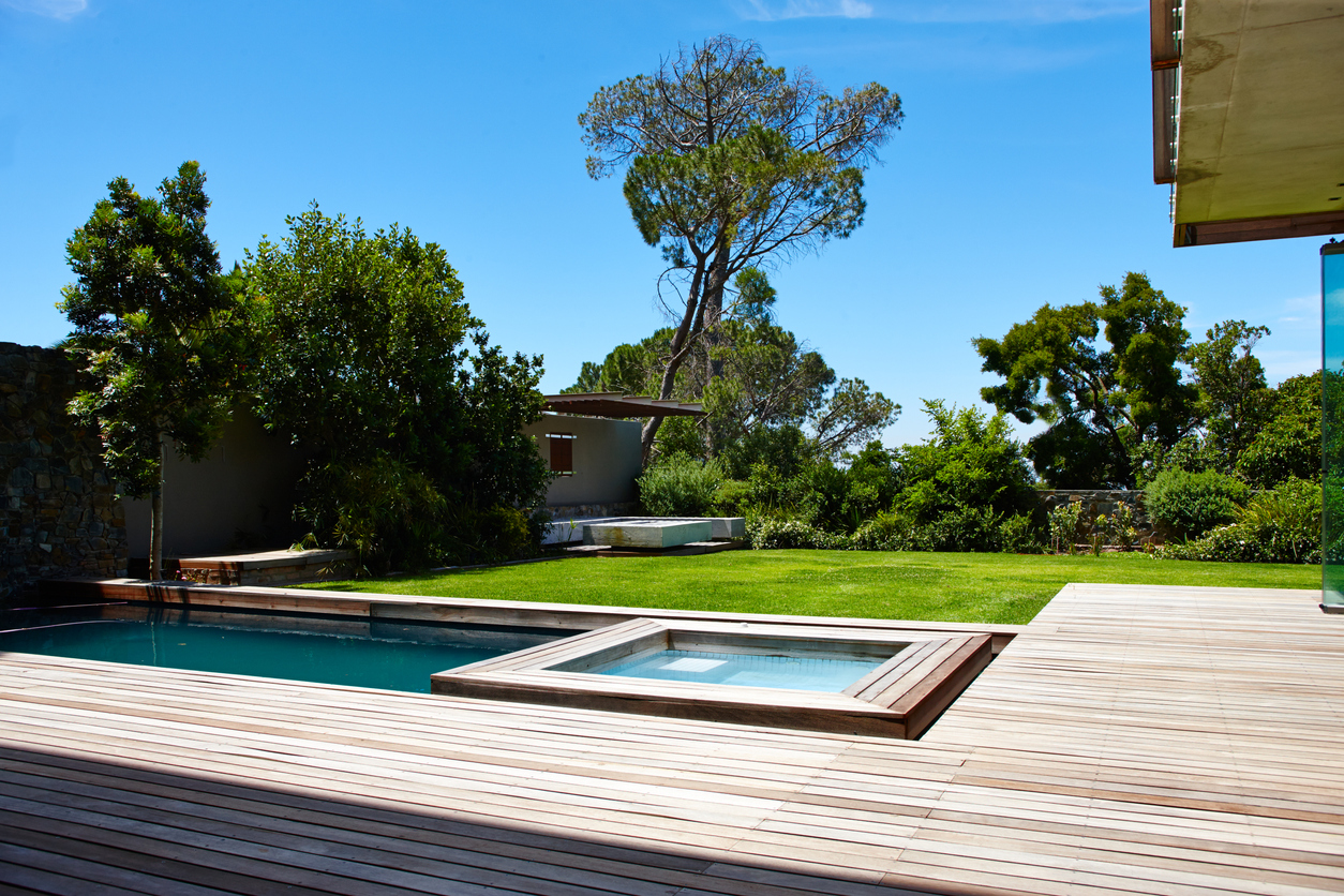 A modern, minimalist wood-slat deck with pool, with a lawn and house in the background.