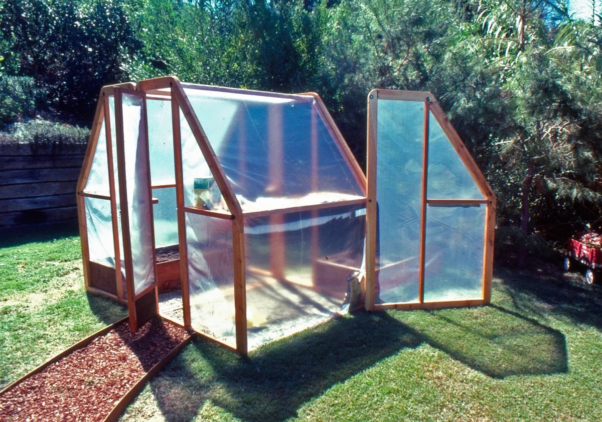 Small greenhouse in yard with plastic sheeting and wood framing.