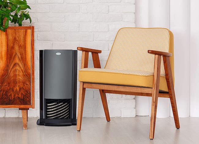 A black evaporative humidifier is on the floor next to a modern wood chair.