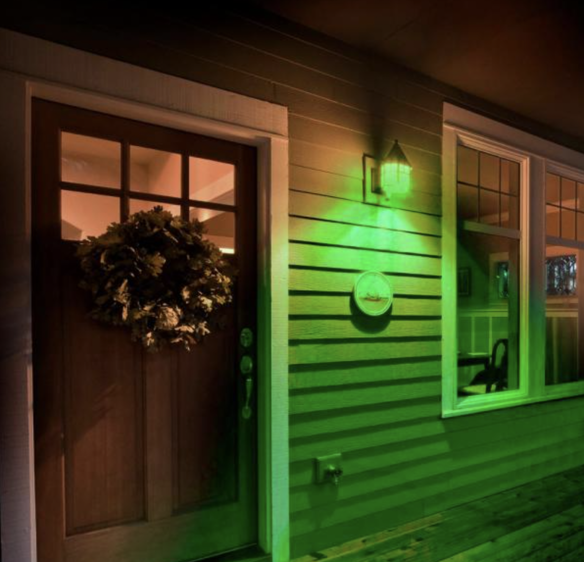 A close up photo of a home's front door and front exterior light, which is illuminated green.