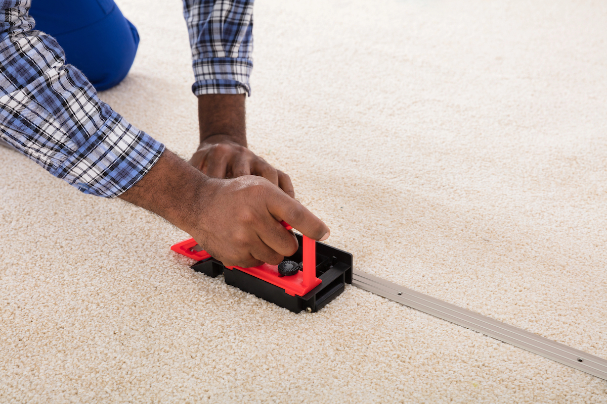 A person is installing white carpet with a tool.