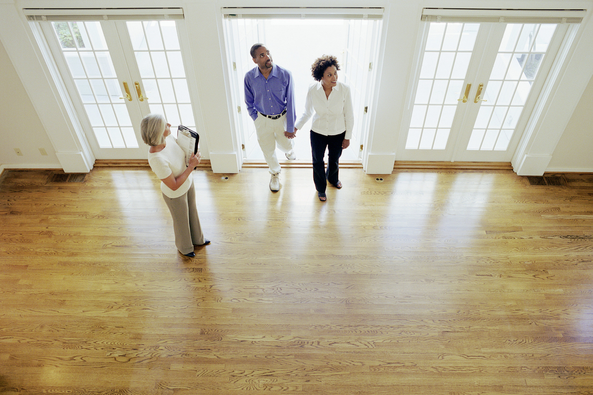 A realtor is showing a couple a home for sale that has hardwood flooring.