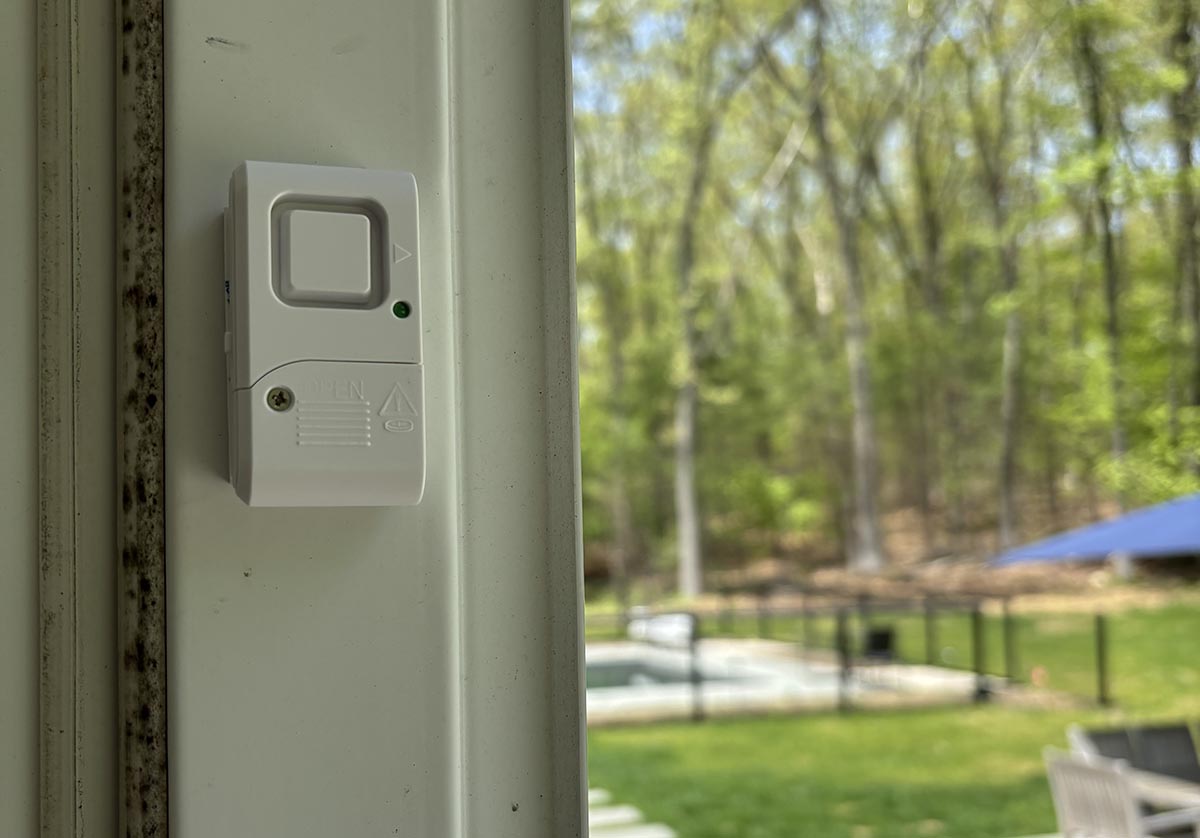 The GE Audible Window/Door Alarm installed on a patio door with a pool in the background.
