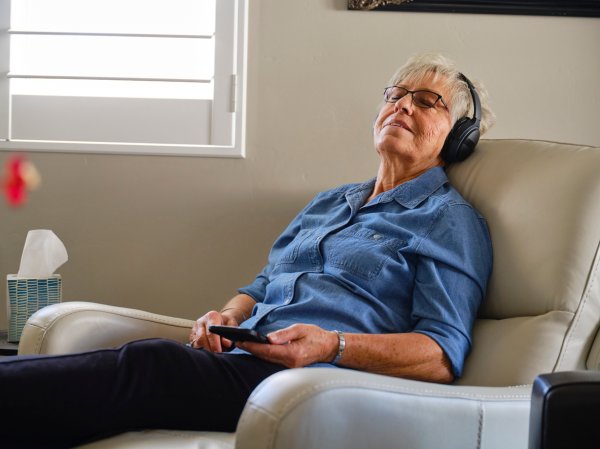 An older woman in the best recliner for sleeping option reclined with eyes closed and listening to headphones