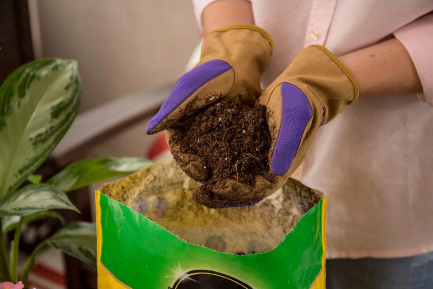 Gloved hands holding potting mix soil above a green bag