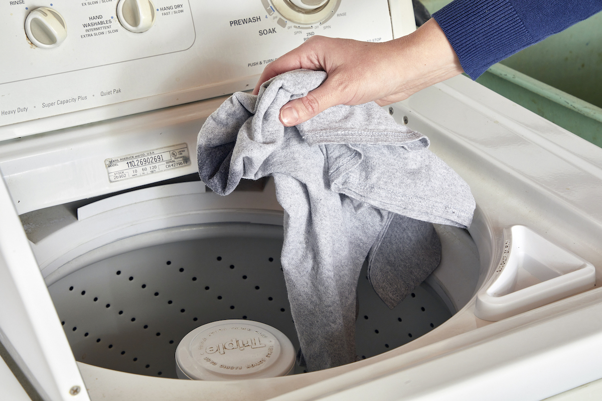 Woman drops clothing into a washing machine.