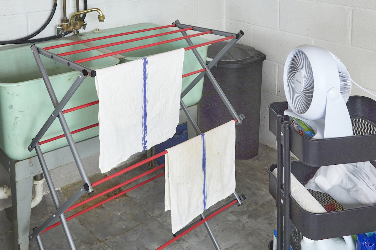 Cloths on drying rack in basement laundry room being dried by a portable fan.