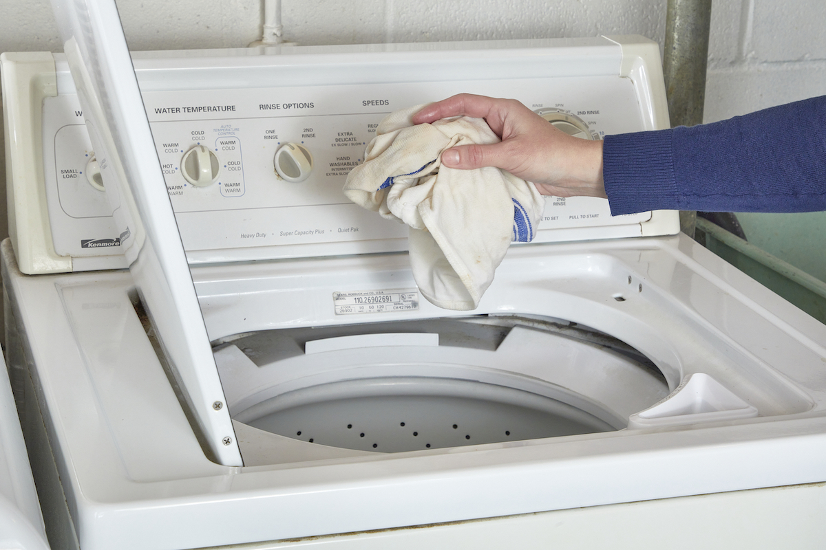 Woman tossing moldy cloth into a washing machine for cleaning.