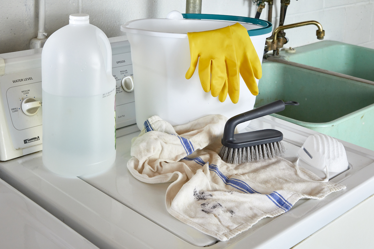 Materials needed for getting mold out of clothes, including rubber gloves, scrub brush, bucket, and vinegar.