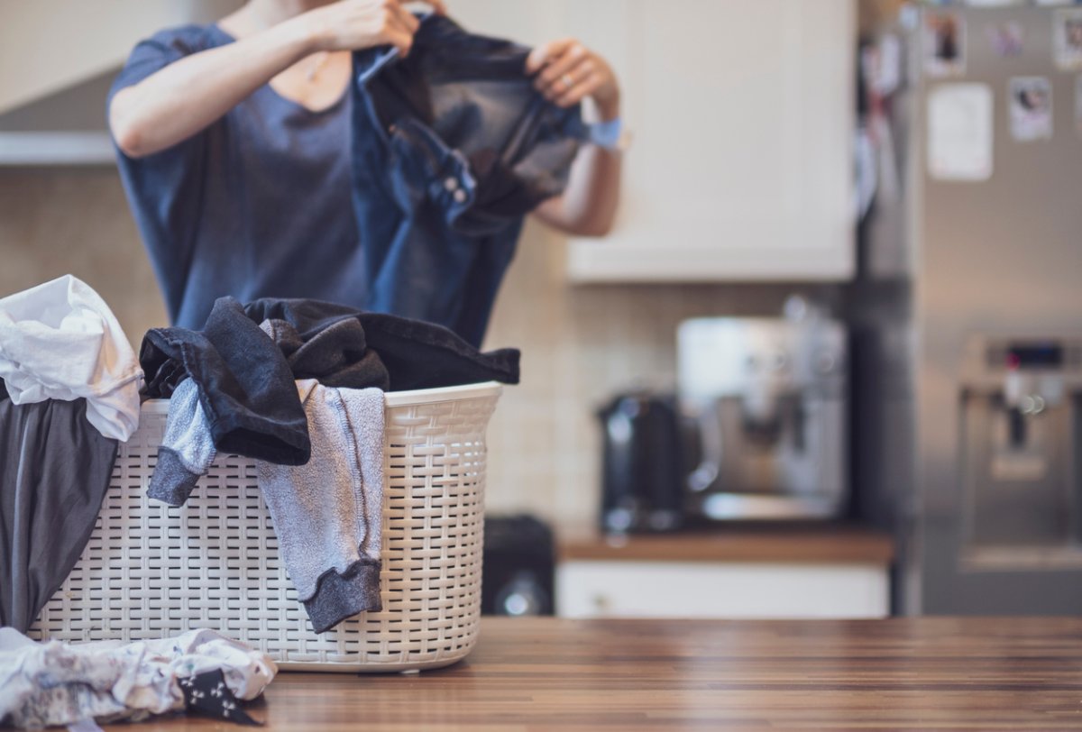 A woman inspects dirty laundry in her kitchen.