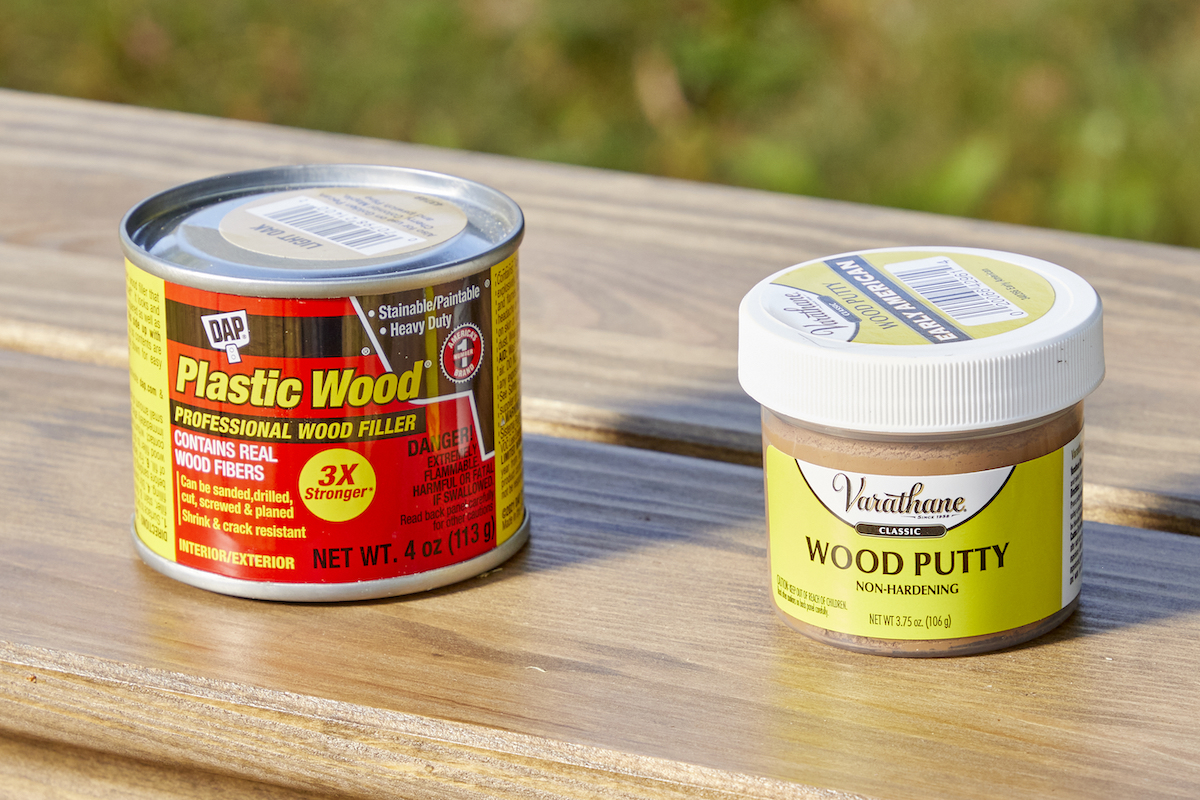 Containers of both wood putty and wood filler on a wooden table.