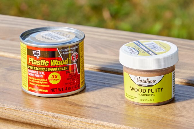 Containers of both wood putty and wood filler on a wooden table.