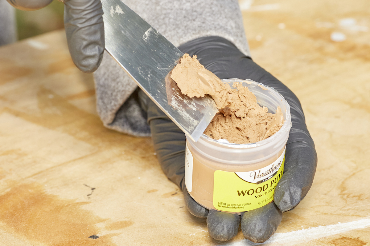 Woman uses a putty knife to scoop out and show color of wood putty.