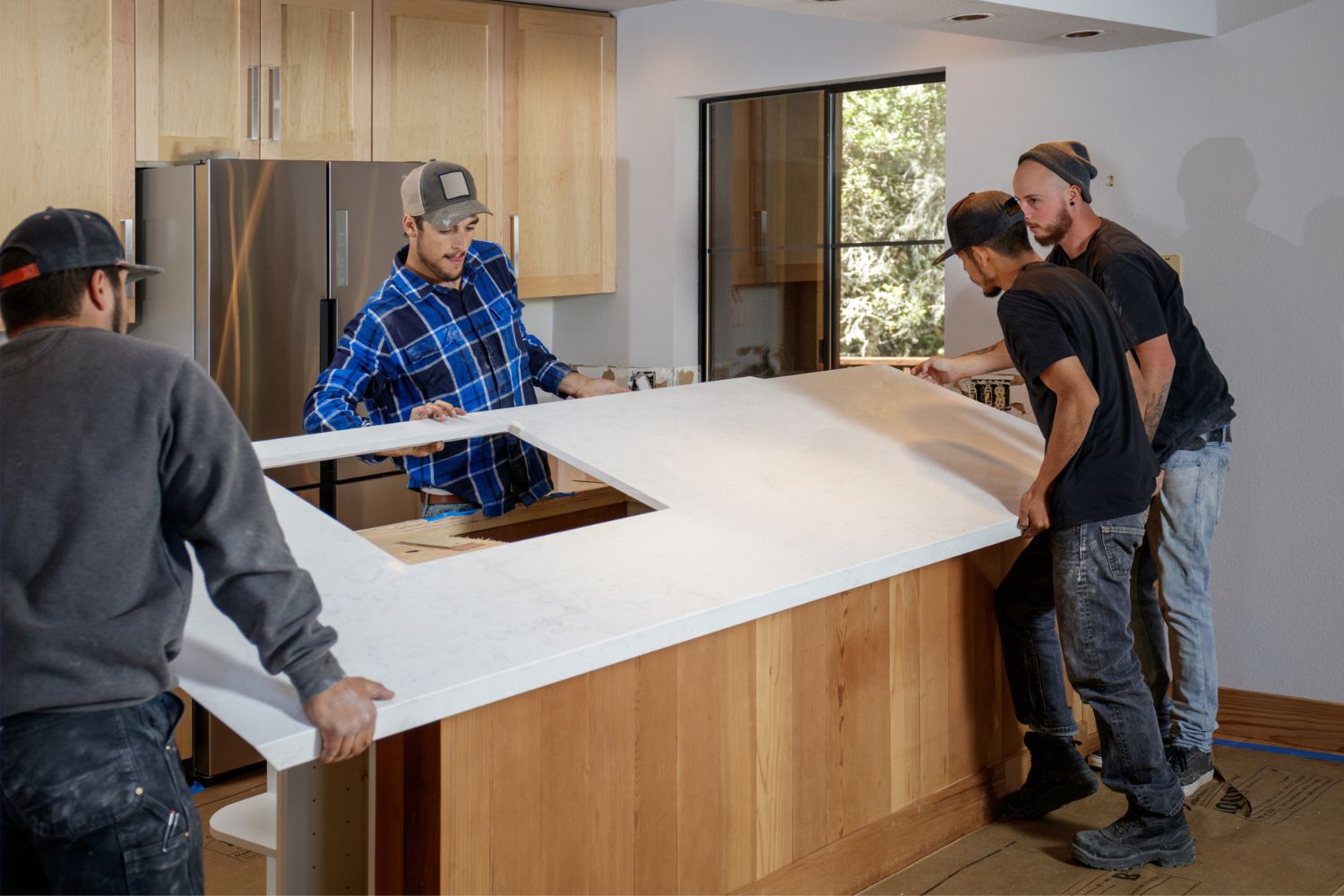 A team of workers place a quartz countertop on a wooden cabinet base in a kitchen.