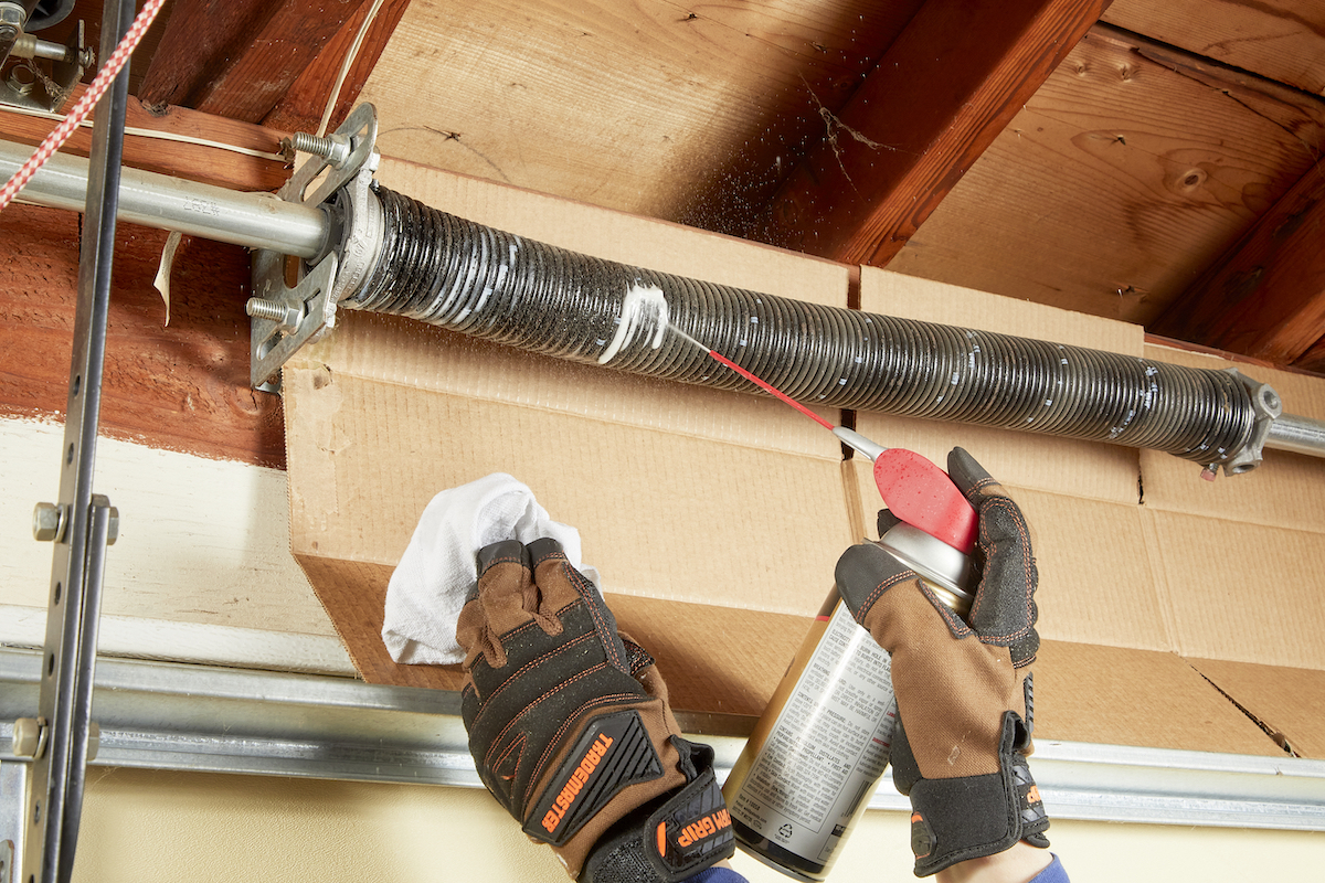 Woman wearing work gloves lubricates garage door springs.