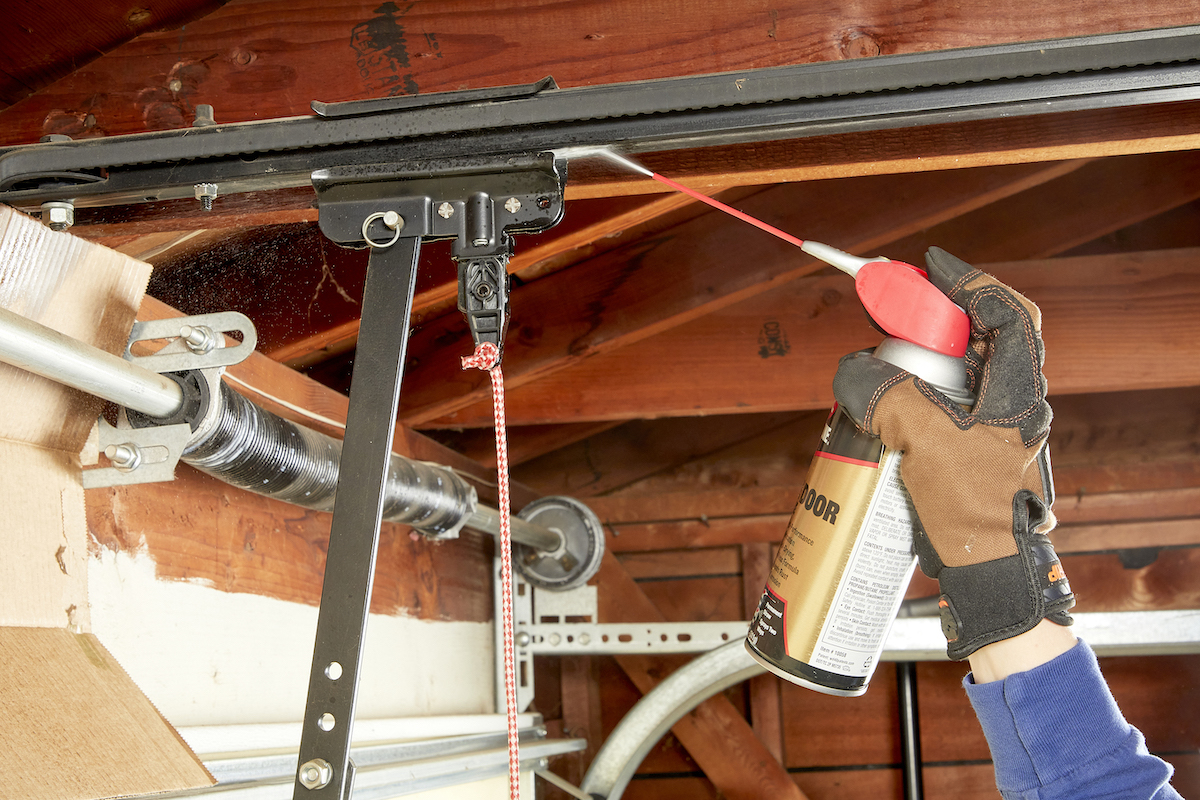 Woman lubricating the top rail of a garage door.