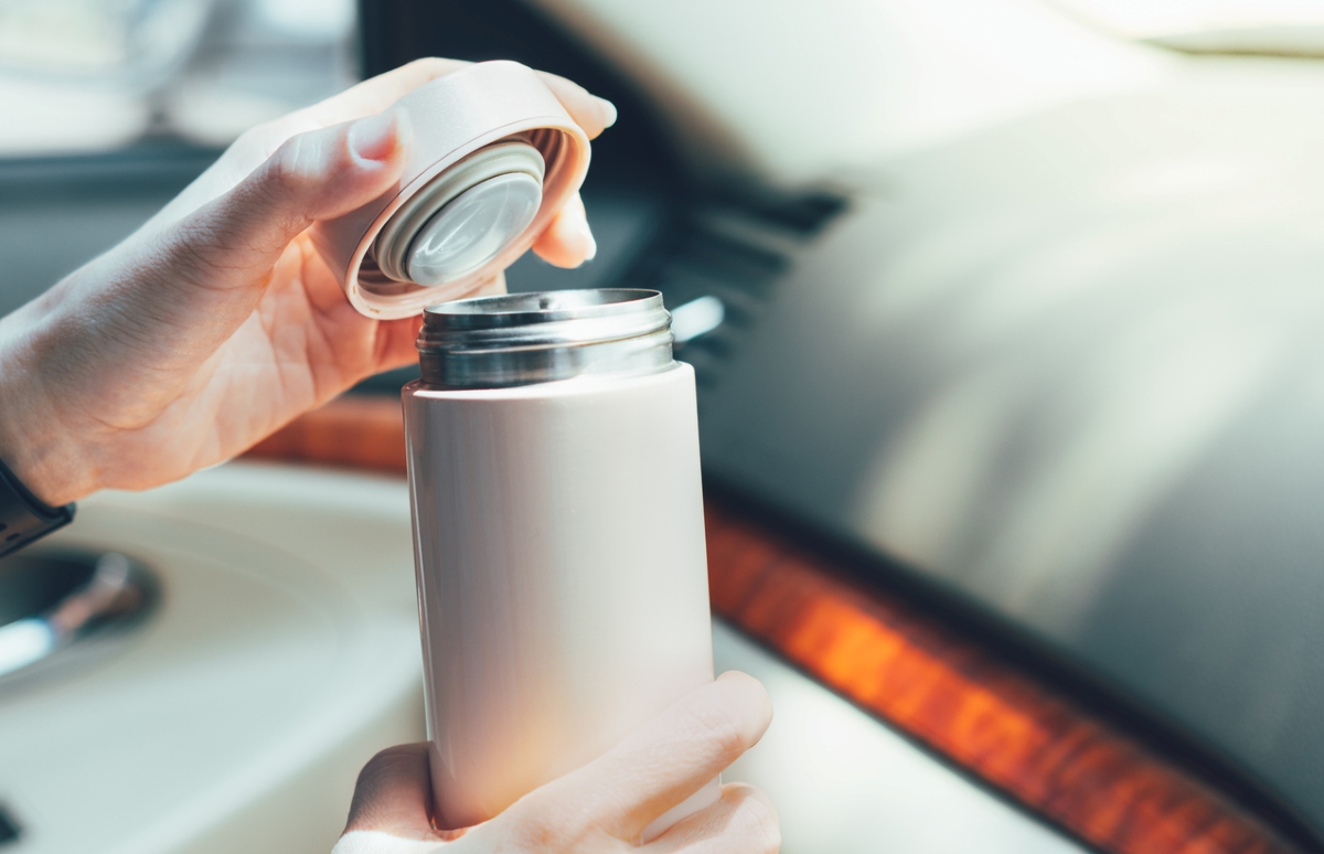 A person opening a grey-colored travel thermos inside car.