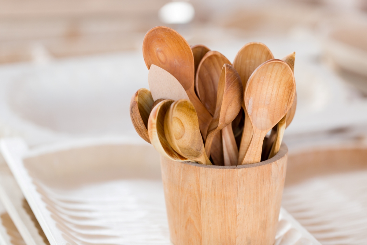 Wooden kitchen utensils in a wooden container next to a kitchen sink.