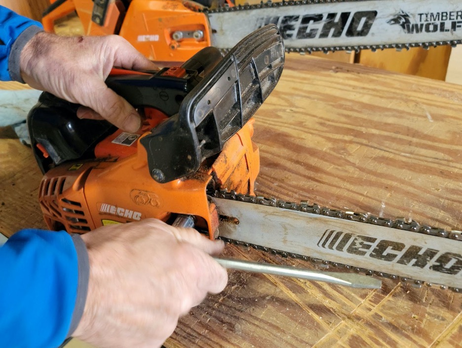 Man loosens the bolts on the side of a chainsaw.