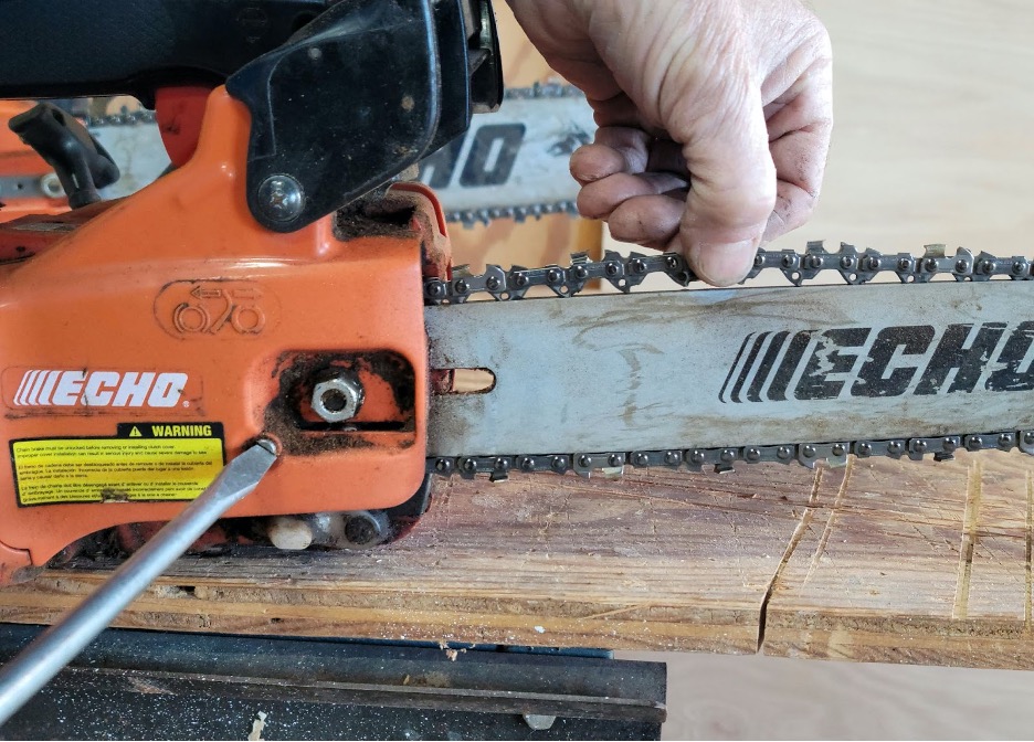 Man holds chainsaw chain in one hand and tightens a screw on the chainsaaw with the other.