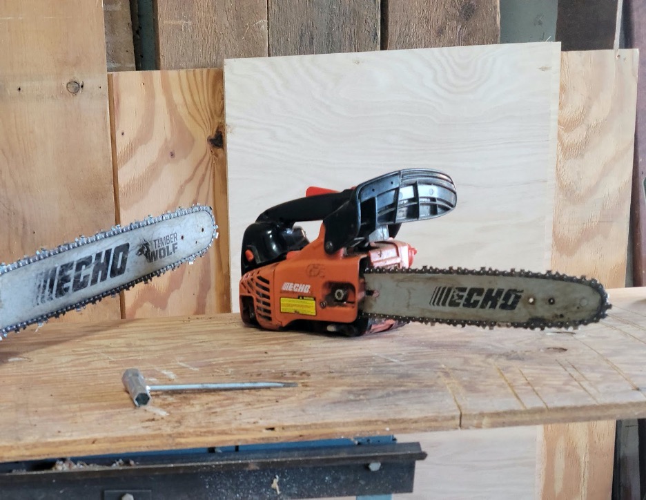 Two chainsaws and a scrench on top of a wooden work table.