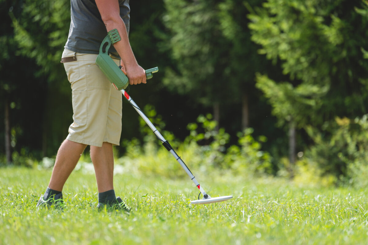 Man uses a metal detector in a grassy yard.