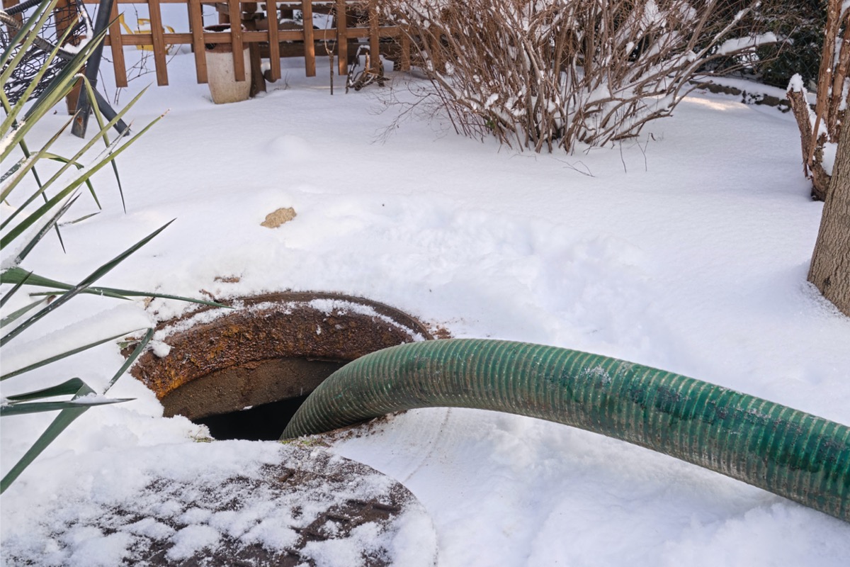 Thick septic hose lowered into a septic tank, surrounded by snow on the ground.